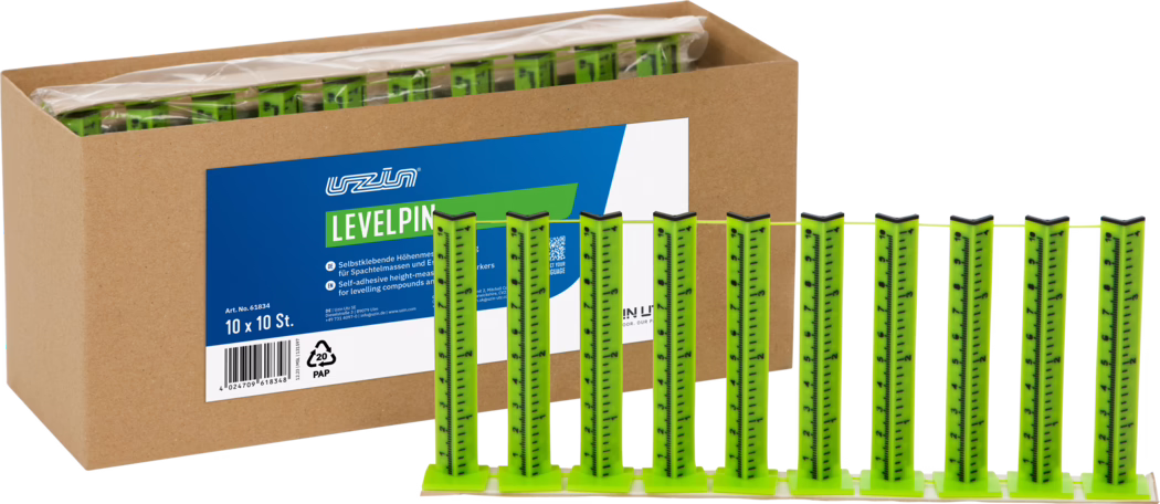UZIN_Dummy_Levelpin_2026-02 A cardboard box containing multiple bright green self-adhesive leveling pins; ten vertical measuring strips connected by a base and a thin yellow string are displayed in front, with a blue-and-white product label on the box reading 'LEVELPIN'.